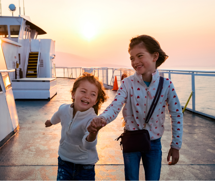 Two girls running laughing on a ferry during a sunset
