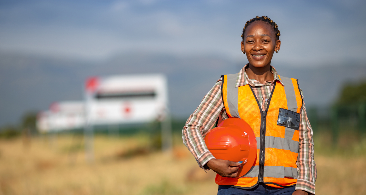 Ivanhoe Mines African female employee holding hard hat wearing a high visibility vest, smiling