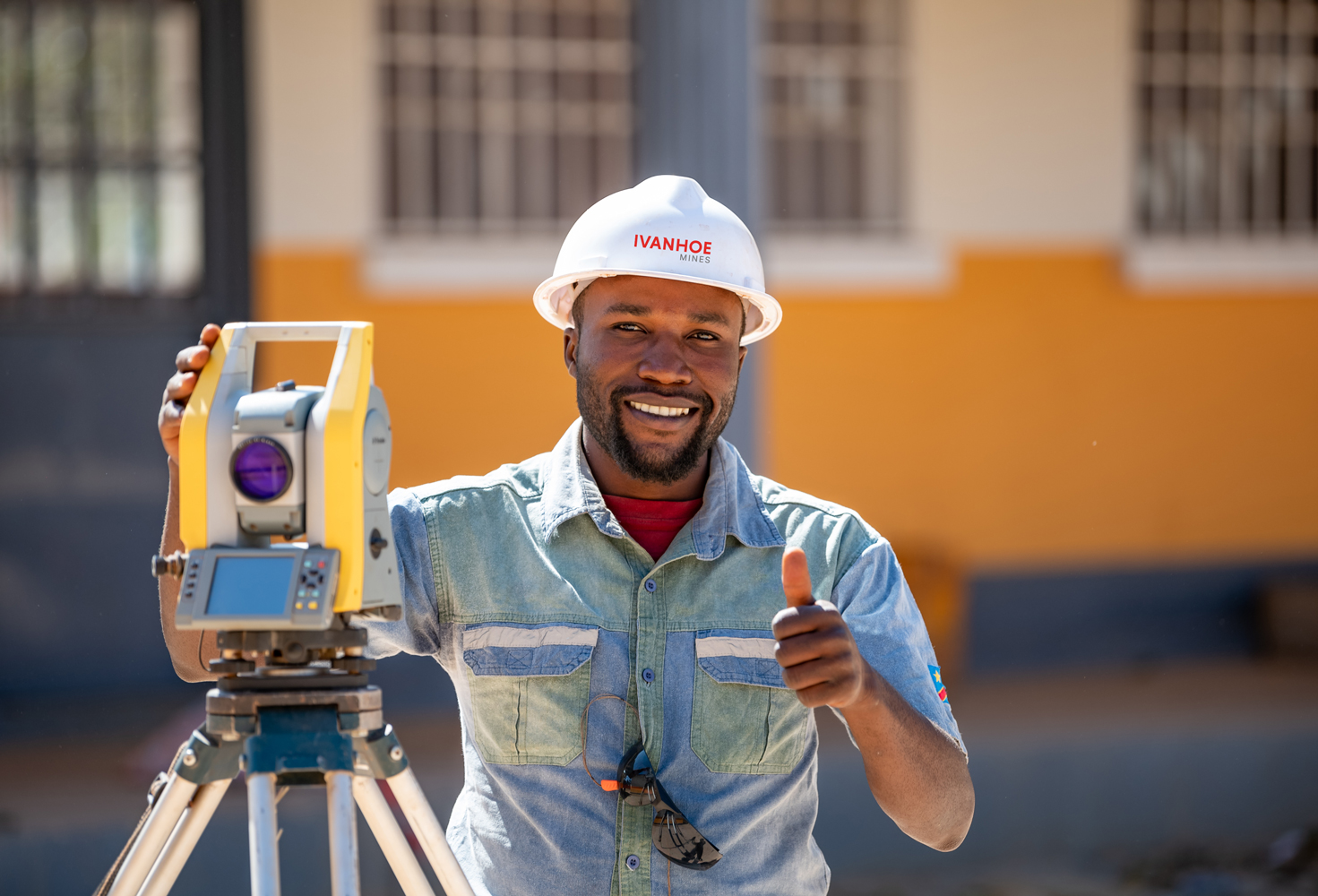 A man with a hard hat standing behind a Laser Measuring Tripod
